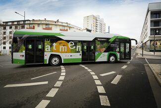 Ein grün-weißer E-Bus biegt um die Kurve.