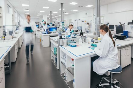 Blick in ein Labor mit mehreren Menschen an weißen Labortischen.