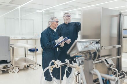 Zwei Menschen in Laborkleidung vor einem Gerät in einem Labor.