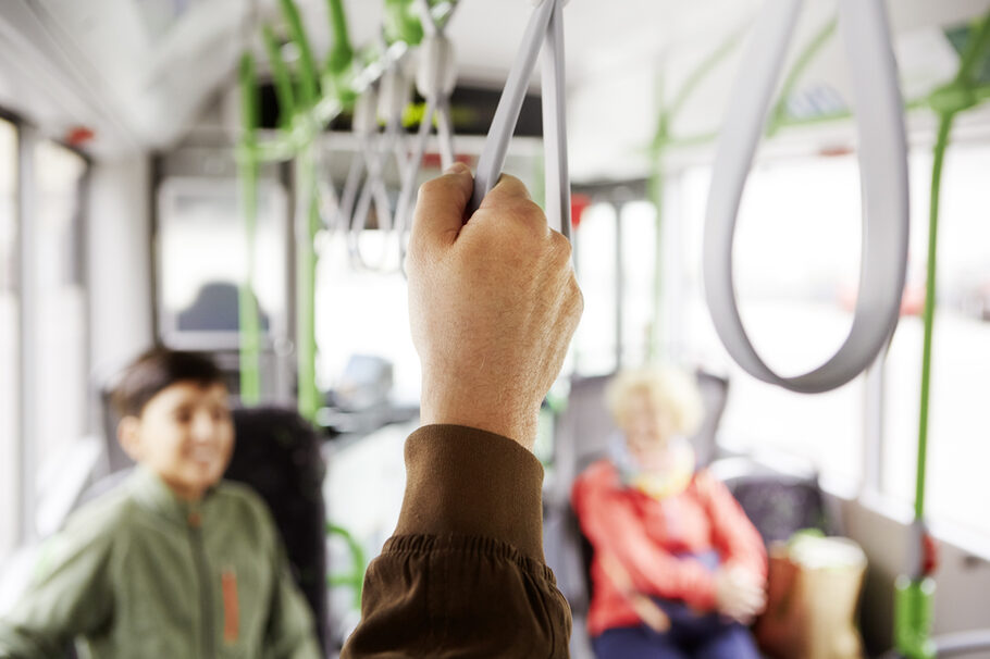 Hand eines Fahrgastes umfasst eine Halteschlaufe in einem Bus.