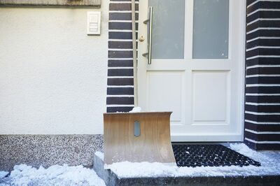 Ein Schneeschieber steht vor einer Haustür.