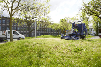 Ein Mitarbeiter des Stadtservice mäht den Rasen auf einem Firmengelände.