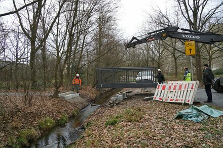 Neue Brücke wird mit einem mobilen Kran über den Hainbach gesetzt.