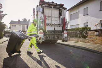 Müllwerker zieht eine Tonne zum Müllfahrzeug