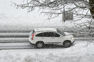 Ein weißes Auto fährt eine schneebedeckte Straße entlang.