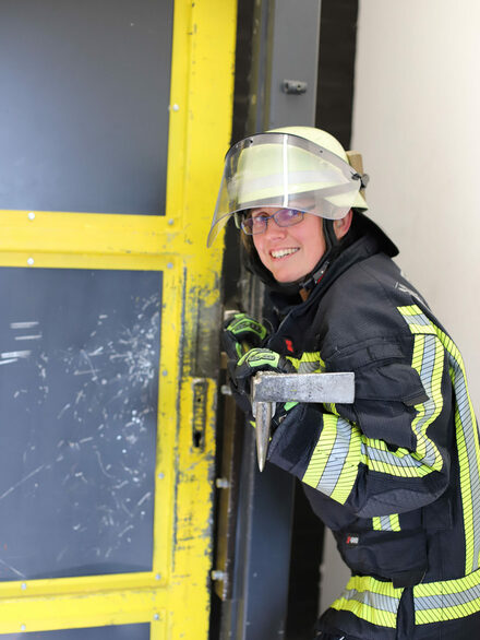 Eine Feuerwehrfrau stemmt eine Haustür auf.
