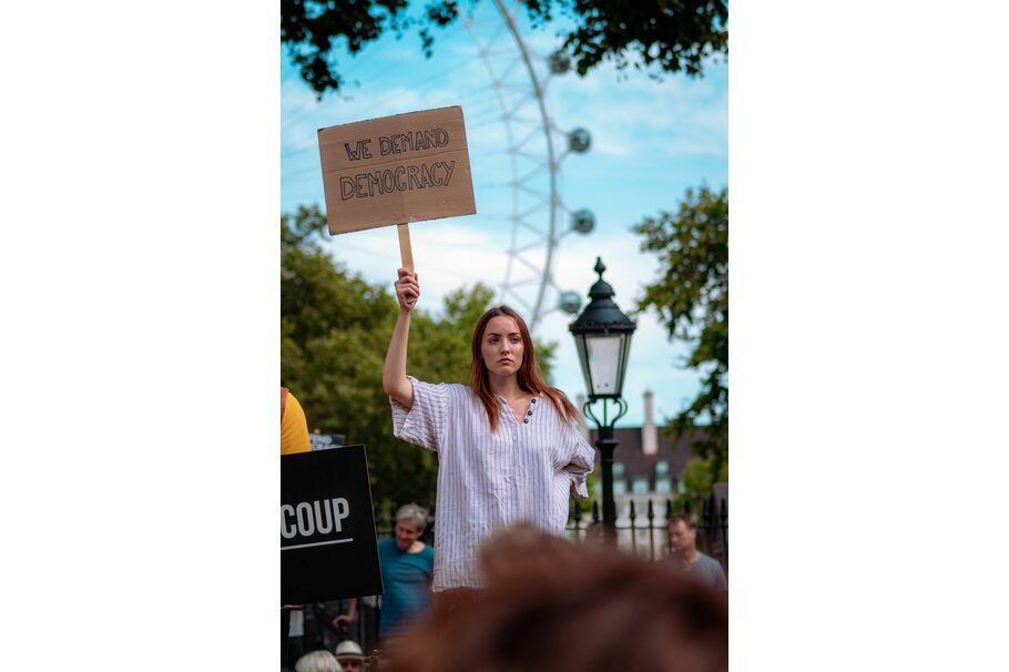 Eine Frau mit einem Protestschild auf dem we demand democracy steht