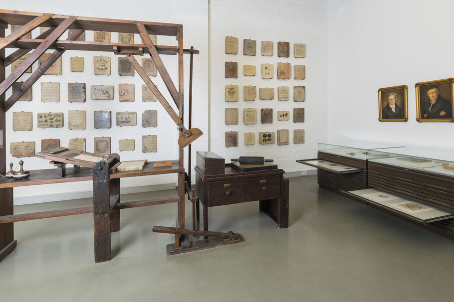 Die lithographische Stangenpresse im Museum mit den Lithographiesteinen und Schaukästen im Hintergrund