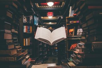 Ein aufgeschlagenes Buch schwebt in einem Lichtkegel zwischen vielen anderen Büchern in einer Bibliothek