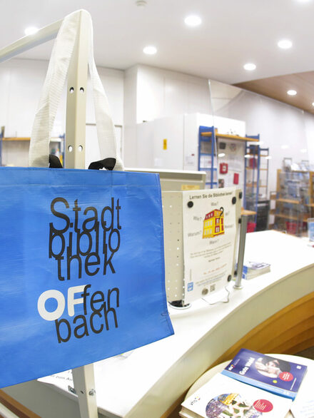 Eine blaue Tasche mit der Aufschrift Stadtbibliothek Offenbach hängt an einem Metallstab.