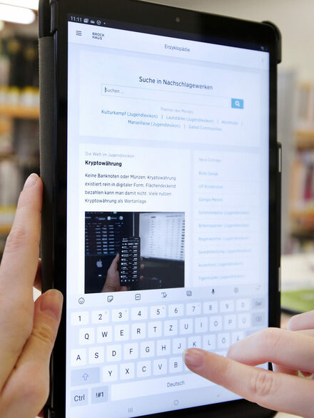 Eine Hand tippt im Textfeld einer Nachschlagewebseite auf einem Tablet.