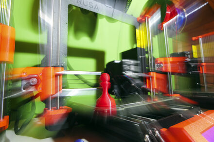 Eine rote Spielfigur steht auf einem 3D-Drucker.
