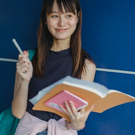 Eine junge Frau hält Bücher in der Hand und lacht.