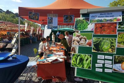 Stand auf dem Wochenmarkt, vorne ein Aufsteller mit dem Marktquiz mit Bildern von Obst und Gemüse