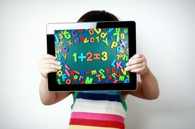 Kind hält Tablet hoch, Bildschirm mit bunten Zahlen und Buchstaben