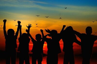 Kinder stehen vor einem Sonnenuntergang und strecken die Arme in die Höhe