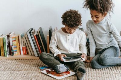 zwei Kinder sitzen vor Büchern und lesen auf einem Tablet