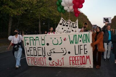 Menschen laufen auf einer Straße und halten ein Plakat mit der Aufschrift "Frau, Leben, Freiheit"