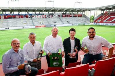 Fünf Männer mit Apfelweinflaschen vor der grünen Rasenfläche des Stadions.
