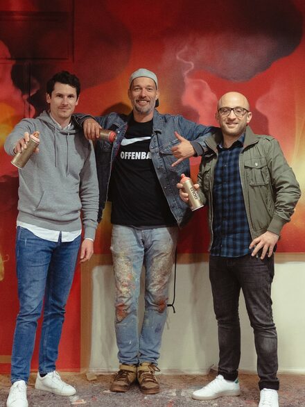 Drei Männer mit Sprühdosen vor dem neuen Graffiti. In der Mitte der Künstler Marcus Dörr.