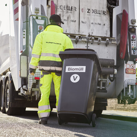 Ein Müllwerker zieht eine Bioabfalltonne zum Müllfahrzeug.