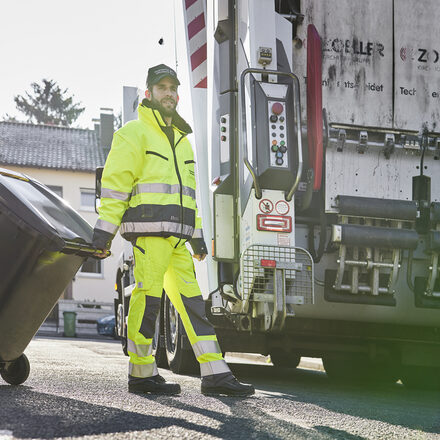 Müllwerker der Stadtwerke bringt eine Tonne zum Abfallfahrzeug.