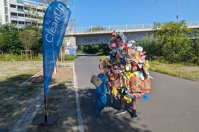 Der personifizierte Abfallhaufen Mülli vor einer Beachflag mit der Aufschrift "MainCleanup".