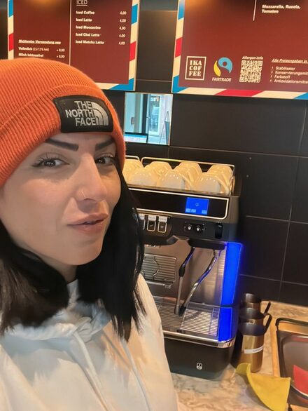 Esma Atay vor einem Kaffeeautomat.
