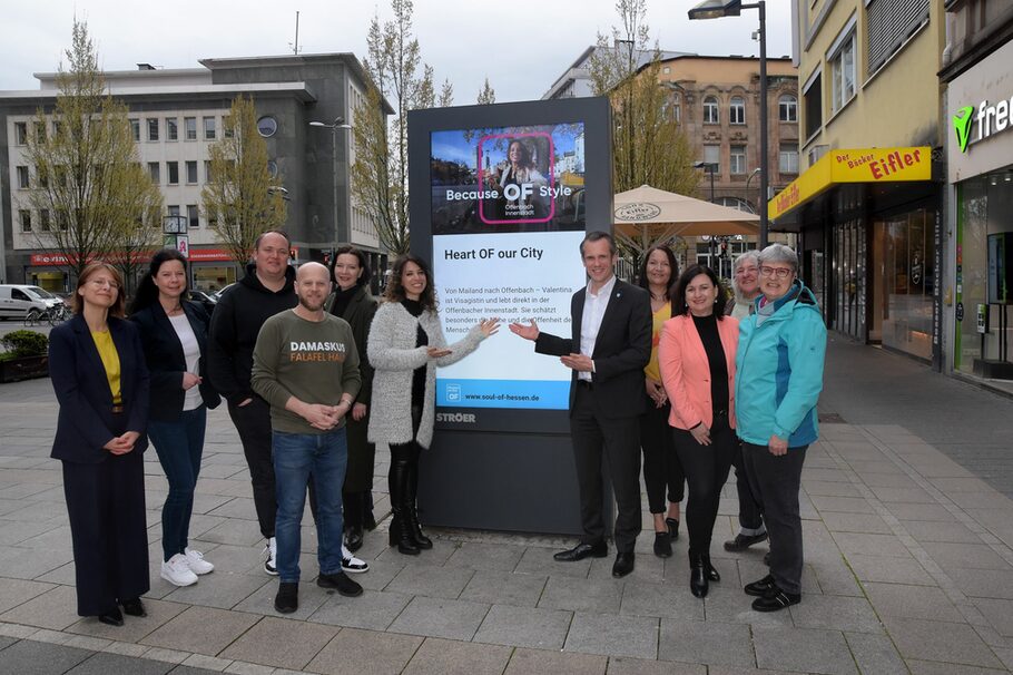 Elf Menschen vor einem digitalen Screen von Ströer, sie zeigen auf das neue Kampagnenmotiv der Innenstadt-Kampagne zu Soul of Hessen.