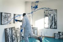 Ein Raum mit vielen Bildern mit einem Mann, der blaue Farbe auf die Wand wirft.