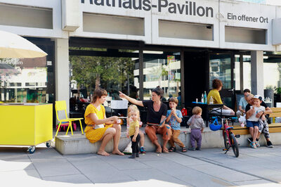 Menschen verschiedener Altersgruppen sitzen vor dem Rathaus-Pavillon