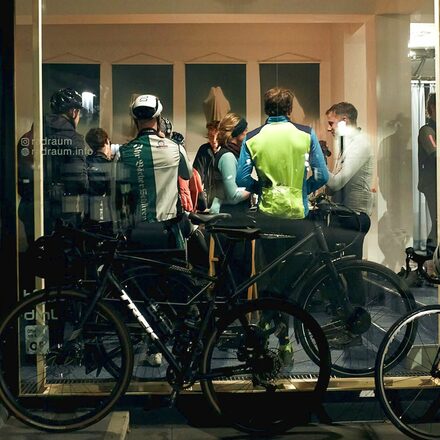 Durch eine Fensterscheibe sieht man Menschen in einem Raum, davor stehen Fahrräder.