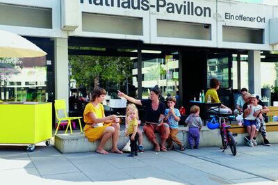Kinder und Erwachsene sitzen vor einem Gebäude und essen Eis.